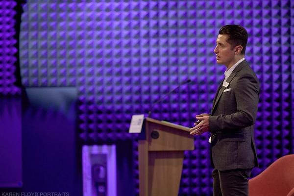 Oscar Mancia, chapter director at large and emerging leader, speaks on stage to a room of more than 100 people at a 2023 event that he created to bridge the innovation gap between industry and government, InnovateGov.